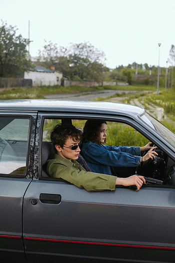 young couple, old car, holding guns, dramatic scene, intense moment, man and woman, car interior, outdoor setting, vintage vehicle, rural background, sunglasses