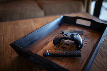 black controller, wooden tray, cozy indoor, rustic tray, game controller, black game controller, indoor setting, wooden surface, remote control, tray with controller, black tray