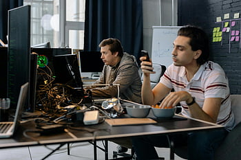 men sitting at table, modern office setup, technology collaboration, two men working, office environment, computer work, professional workspace, teamwork, modern workspace, office technology, focused work
