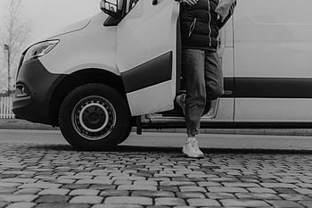 grayscale photo, man getting out, vehicle, monochrome image, person stepping, van, cobblestone pavement, black and white, outdoor scene, urban setting, transportation