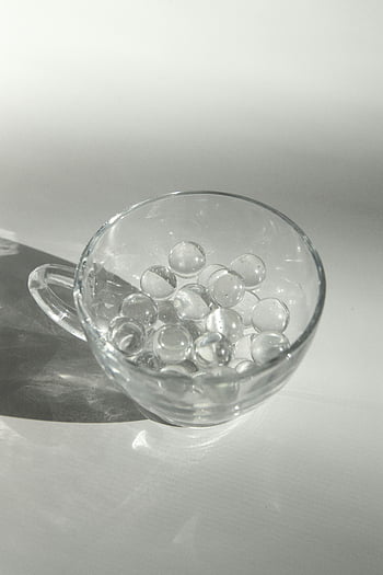 glass cup, transparent balls, white surface, elegant glass, transparent spheres, soft daylight, harmonious shadow, glass mug, clear marbles, minimalistic design, modern decor