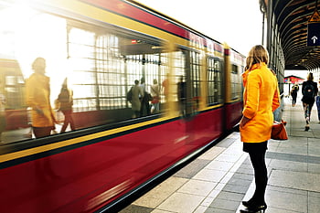 woman, yellow coat, red train, bustling station, train station, waiting, passenger, urban, transportation, public transit, motion blur