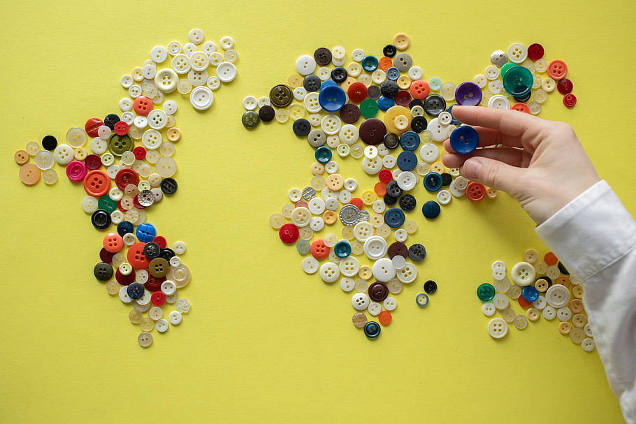 colorful buttons, world map, assorted buttons, vibrant yellow background, button collection, hand arranging buttons, creative art, craft project, decorative buttons, unique design, DIY art