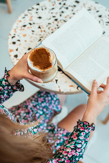 wanita membaca, es latte, Kafe yang semarak, Book, kopi, meja kafe, menikmati latte, gaun bunga, tampilan overhead, momen yang nyaman, waktu membaca