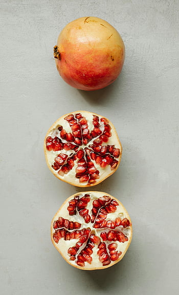 ripe pomegranates, gray background, vibrant seeds, overhead shot, whole pomegranate, sliced pomegranate, red seeds, fruit photography, healthy food, fresh pomegranate, food styling