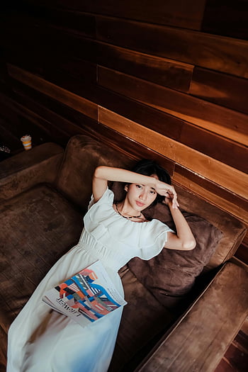 Žena v bílých šatech, ležet na gauči, hnědý gauč, Modní časopis, uvnitř, příležitostná pozice, uvolněné nastavení, moderní interiér, Stylový outfit, pohodlné nastavení, žena čtení časopis
