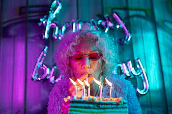nonna chic, Donna senior alla moda, Candele di salto, Celebrazione vibrante di compleanno, luci al neon, torta di compleanno, nonna elegante, nonna moderna, festa colorata, moda senior, festa di compleanno