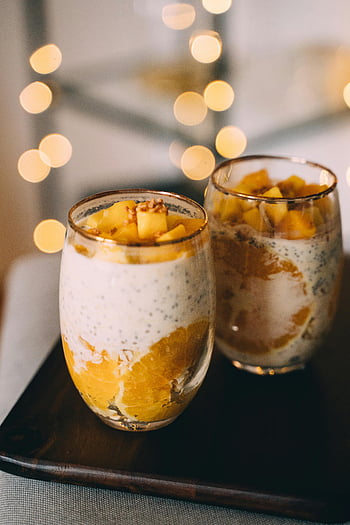 Budinca de mango chia, budincă de chia portocalie, pahare cu budincă de chia, tavă din lemn, felii de mango proaspete, felii de portocale, budincă de chia stratificată, budincă vibrantă de chia, ochelari elegant, desert sanatos, budincă de chia cu fructe