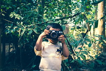 Boy, Holding, Black Flash Camera, Green Leaf Plants, young child, vintage camera, exploring outdoors, Indian forest setting, nature photography, outdoor adventure, childhood memories