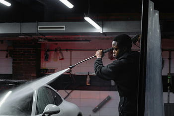 car wash, high-pressure hose, indoor garage, man in black jacket, spraying water, car cleaning, auto detailing, vehicle maintenance, pressure washing, car service, garage setting