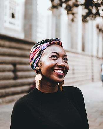 woman wearing headscarf, vibrant headscarf, smiling woman, urban street setting, earrings, colorful headscarf, outdoor portrait, city background, fashion accessory, street style, cultural attire