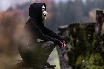 kerel fawkes masker, zwarte hoodie, bosrijke omgeving, buitenshuis, donkere atmosfeer, raadselachtig, persoon zitten, wit masker, anoniem, figuur met een kap, natuur achtergrond