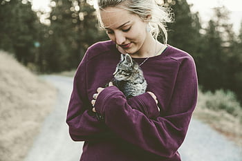 purple sweater, silver tabby cat, young woman, outdoors, pathway, selective focus, kitten, smiling, holding cat, nature, forest background