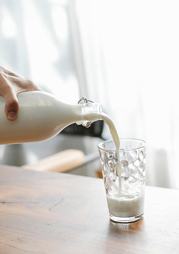 pouring milk, glass of milk, wooden table, bright indoor, fresh milk, hand pouring, milk bottle, milk glass, indoor setting, milk pouring, glass on table