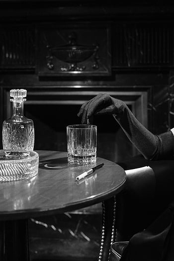 monochrome photo, woman's fingers, drinking glass, black gloves, vintage noir, mysterious woman, table setting, crystal decanter, black and white, retro style, noir atmosphere