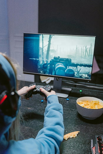 gamer, fekete játékvezérlő, fókuszált játékos, lövöldözős játék, monitor, harapnivalók a közelben, játék életmódja, Videojátékok lejátszása, játék beállítás, szórakozás, beltéri játék