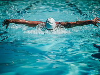 butterfly stroke, swimmer, swimming pool, powerful stroke, splashing water, swim cap, aquatic sport, competitive swimming, swim technique, water sport, pool activity