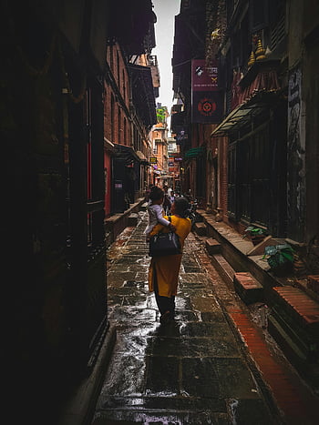 woman carrying girl, concrete building, daytime, narrow alleyway, historic alleyway, family moments, mother carrying child, urban scene, street photography, cultural setting, daily life