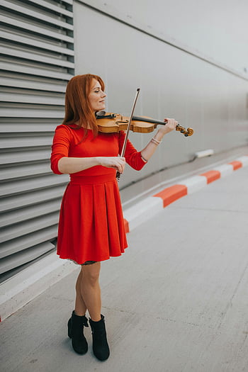 woman in red dress, playing violin, outdoors, modern building, street performance, musician, red dress, violinist, urban setting, performance art, red-haired woman