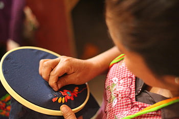 woman sewing, blue textile, embroidery patterns, traditional craftsmanship, colorful patterns, fabric hoop, skillful embroidery, textile art, cultural craft, hand embroidery, needlework