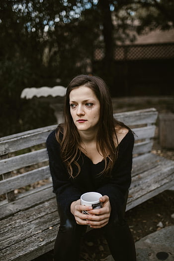 Weinende Frau, Holzbank, Keramikbecher, Herbsttag, In Gedanken verloren, Outdoor-Einstellung, emotionaler Moment, Kontemplative Stimmung, natürliches Licht, Gelassene Umgebung, Fotografie im Freien