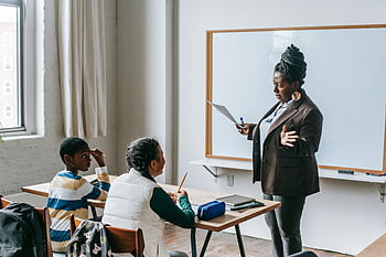 Black teacher, diverse classroom, elementary pupils, whiteboard, engaging students, presentation, education, teaching, classroom setting, multi-ethnic students, teacher explaining